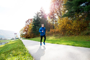 Young athlete running in park in colorful autumn nature.