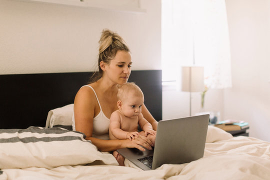 Baby girl and mother sitting up in bed staring at laptop