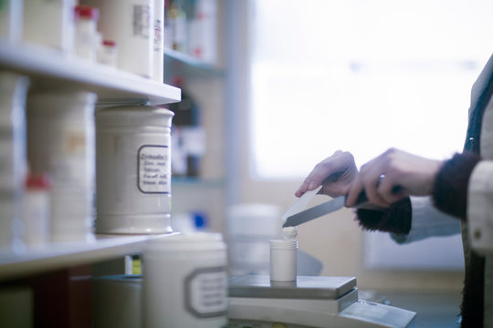 Male pharmacist weighing medical drug on pharmacy scales, cropped