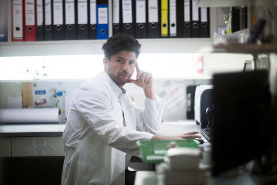 Portrait of young male pharmacist at desk using computer in pharmacy