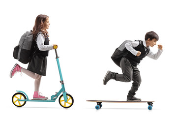 Full length profile shot of a schoolgirl riding a scooter and a schoolboy riding a longboard