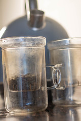 Making tea (green tea leaves) in a glass cup, wit two pieces, green tea leaves with hot water in a transparent clear cup with a kettle near it, making tea with kettle