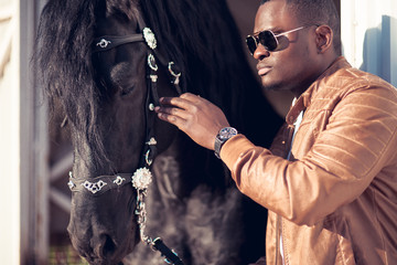 african Man wearing sunglasses near a black horse in hangar