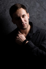 Fototapeta premium Portrait of a handsome muscular guy on a black background in a shirt. Adjusting the shirt. Black shirt. Force.