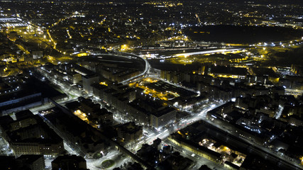 Fototapeta na wymiar Panoramic night aerial view of the Tuscolana district, in the city of Rome in Italy. The streets and buildings are illuminated by street lamps and car headlights.