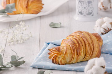 Delicious continental breakfast with fresh flaky french croissants, close up on the croissants. With white cotton flowers on a light wooden background. Provence rustic style
