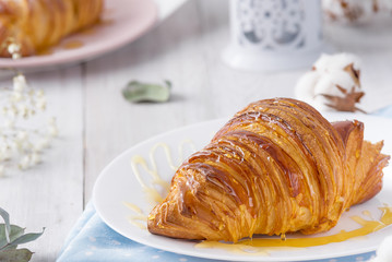Delicious continental breakfast with fresh flaky french croissants whith honey, close up on the croissants. With white cotton flowers on a light wooden background. Provence rustic style