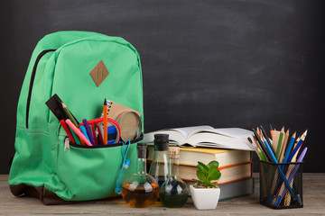 Education concept - school backpack with books and other supplies, blackboard background