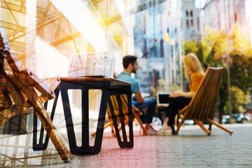 Pleasant cafe. Relaxed young people sitting in a quiet little cafe and having a pleasant talk while a modern computer standing on the table and waiting for the owner