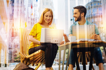 Enthusiastic people. Cheerful pleasant young specialists feeling glad while sitting outdoors in a comfortable cafe and smiling while working at their amazing project