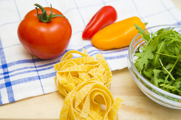 Set of raw ingredients for Italian cooking on a tablecloth background. Salad, tomatos, red and yellow papper, pasta. Set of healthy food products. Closeup