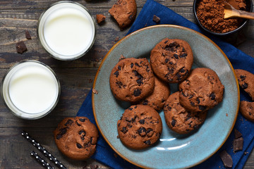 Homemade chocolate cookies in a plate with milk on a wood background.