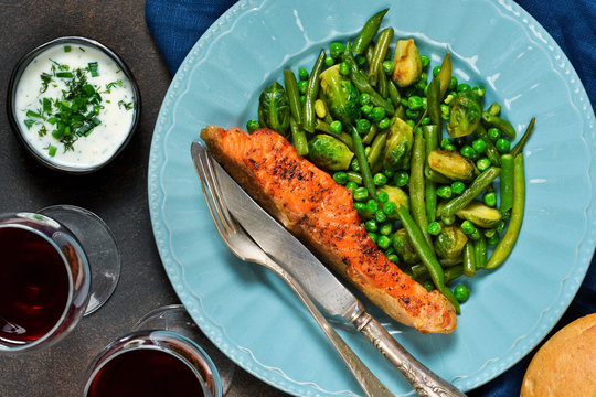 Baked salmon steak with asparagus, Brussels sprouts and green peas on a concrete background with a glass of wine.