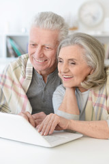  beautiful senior couple with blanket using laptop at home