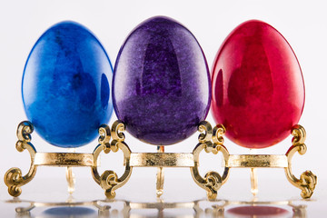 Three marble textured stone easter eggs on gold stands for eastern holiday in purple, blue and red. - 192002410