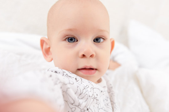 Adorable baby boy with blue eyes looking directly at camera trying to reach for it. Cute toddler close up portrait.