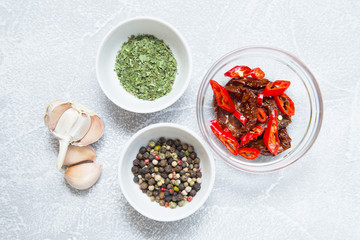 Set of raw ingredients for Italian cooking on stone table background. Black papper, sun dried tomatos, green dry species. Set of healthy food products. Closeup