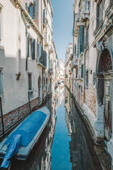A small blue boat tied to a house with a brick wall in a narrow canal, Venice, Italy
