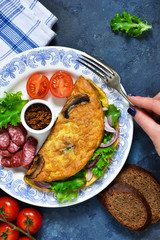 Omelette with mushrooms, cheese and spinach on a concrete blue background. Light breakfast with salami, scrambled eggs and vegetables.