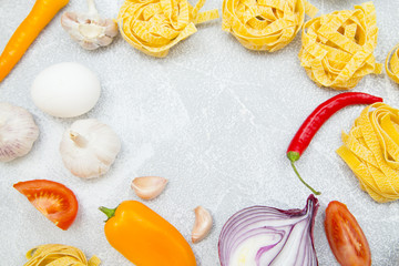 Set of raw ingredients for Italian cooking on stone table background. Red and yellow pappers, garlic, onion, pasta, eggs. Closeup and top view