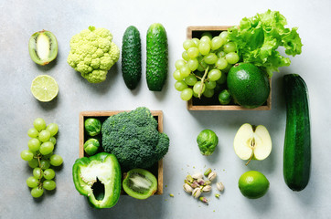 Organic green vegetables and fruits on grey background. Copy space, flat lay, top view. Green apple, lettuce, zucchini, cucumber, avocado, kale, lime, kiwi, grapes, banana, broccoli