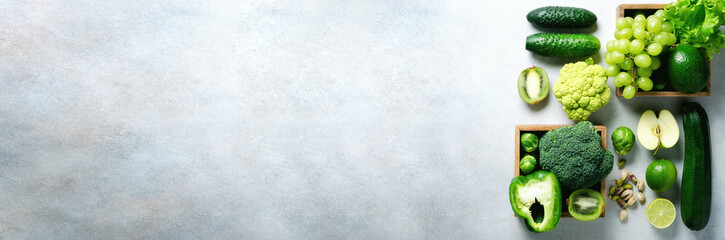 Organic green vegetables and fruits on grey background. Copy space, flat lay, top view. Green apple, lettuce, zucchini, cucumber, avocado, kale, lime, kiwi, grapes, banana, broccoli. Banner