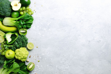 Organic green vegetables and fruits on grey background. Copy space, flat lay, top view. Green apple, lettuce, zucchini, cucumber, avocado, kale, lime, kiwi, grapes, banana, broccoli