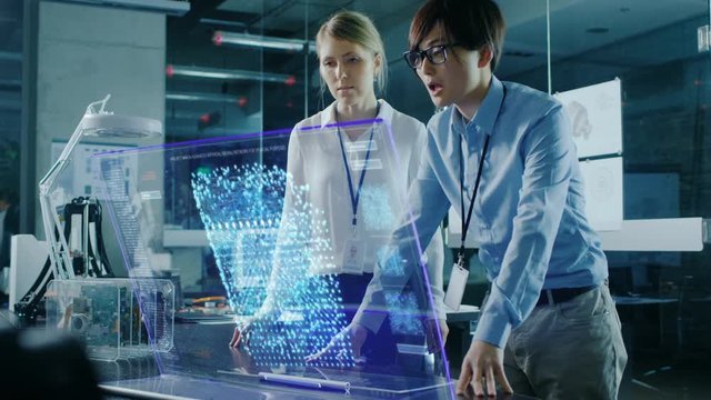 Male and Female Engineers Have Discussion while Using Modern Computer With Transparent Holographic Display. Monitor Shows User Neural Network Architecture Visualization.