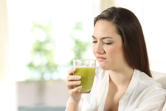 Disgusted woman tasting a vegetable juice with bad flavor