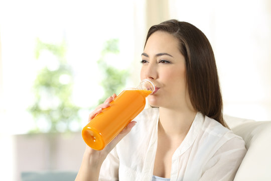 Woman drinking orange juice from a bottle at home