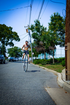 Tattooed young man cycling suburban road on penny farthing