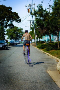 Rear view of tattooed young man cycling suburban road on penny farthing