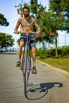 Portrait of tattooed young man cycling suburban road on penny farthing