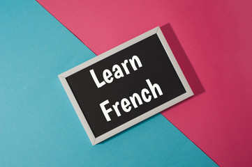 Learn French - text on chalkboard on blue and pink bright background.