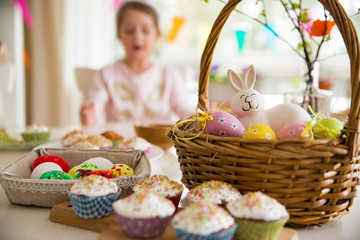 Easter celebration, close-up table with glazed cupcakes, basket with Easter eggs and bunny. Happy family holiday. 