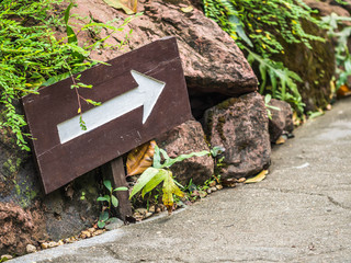 Brown wooden straight arrow sigh or symbol in the park or garden with rocks and cement pavement.