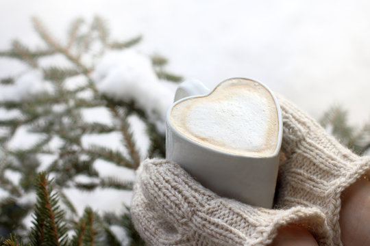  warming moments of winter holidays/ frothy coffee in a mug shaped like a heart, in the hands that are dressed in mittens