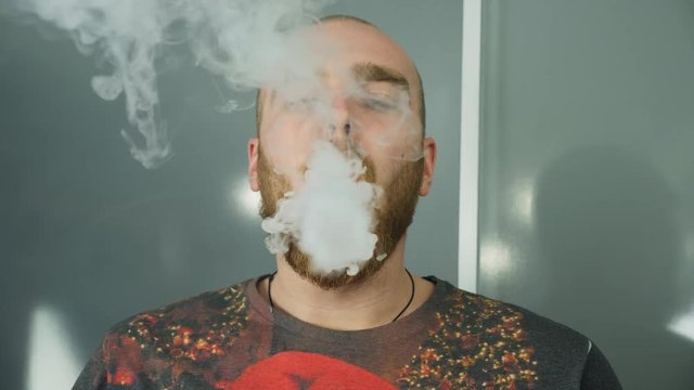 Young man with beard vaping an electronic cigarette. Vaper hipster smoke vaporizer in slow motion. A man's mouth creates smoke rings