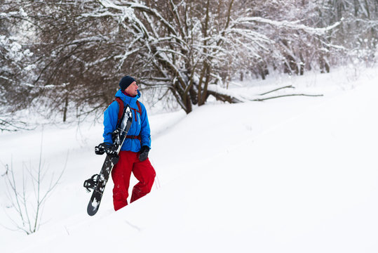 Happy snowboarder stands in the winter forest, admiring winter landscape