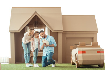 beautiful family with adorable labrador puppy in front of cardboard house isolated on white