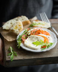 Sliced Italian cheese Mozzarella with a fresh arugula, tomatoes, olive oil, pesto sauce and bread toasts on a wooden box.  Atmospheric photo with hands Place for text. Mmm, yummy.) top view