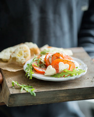 Hearts of sliced Italian cheese Mozzarella with a fresh arugula, tomatoes, olive oil, pesto sauce and bread toasts on a wooden box.   Atmospheric romantic food photo with hands  Restaurant concept.