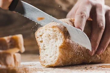 Fotobehang Brood Volkorenbrood op een houten keukenplaat met een chef-kok die een gouden mes vasthoudt om te snijden.