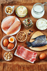 Top view of high-protein products. Milk, cottage cheese, eggs, fish and chicken meat, beans, chickpea and nuts on wooden table.