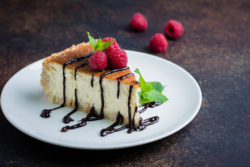 Homemade cheesecake with fresh raspberries and mint decorated with chocolate on plate on dark table background . Healthy organic dessert. Vanilla Cheese Cake. Copy space