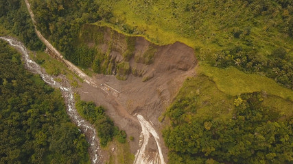 Fototapeta premium Osuwiska i osuwiska na drodze w górach, Camiguin. Widok z lotu ptaka: błoto i skały blokujące drogę. Zniszczone osuwisko drogi wiejskiej uszkodzone w potężnej powodzi. Zawalił się na górze
