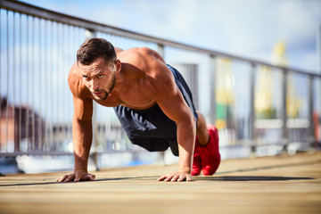 Determinated and athletic man doing pushups shirtless during workout in the city