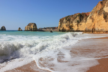 Fototapeta na wymiar Pinhao Beach Summer Scene with Waves at Algarve Coast, Lagos, Portugal. Stones and Cliff Rocks Ocean Shore, Scenic Nature Landscape on Sunny Day. Low Angle Scenic Image of Empty Tropical Lagoon Beach.