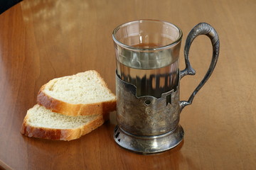 Faceted glass of hot water for tea in an ancient silver cup holder and two slices of bread