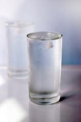 Glass of cold water with ice on blur background